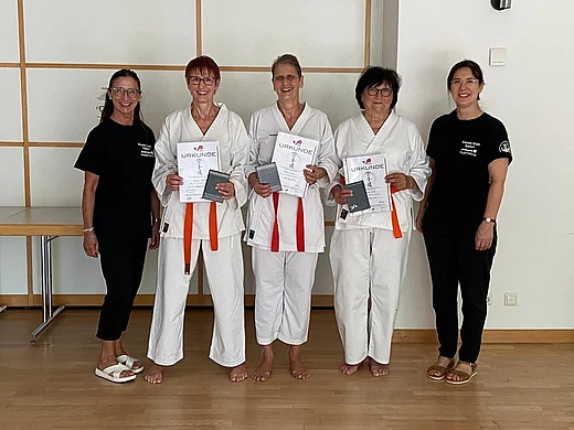 Das Bild zeigt drei Frauen in Karatekleidung, die ihre Uhrkunden zur erfolgreich absolvierten Karateprüfung in den Händen halten. Links und rechts stehen die beiden Trainierinnen in schwarzer Sportkleidung.