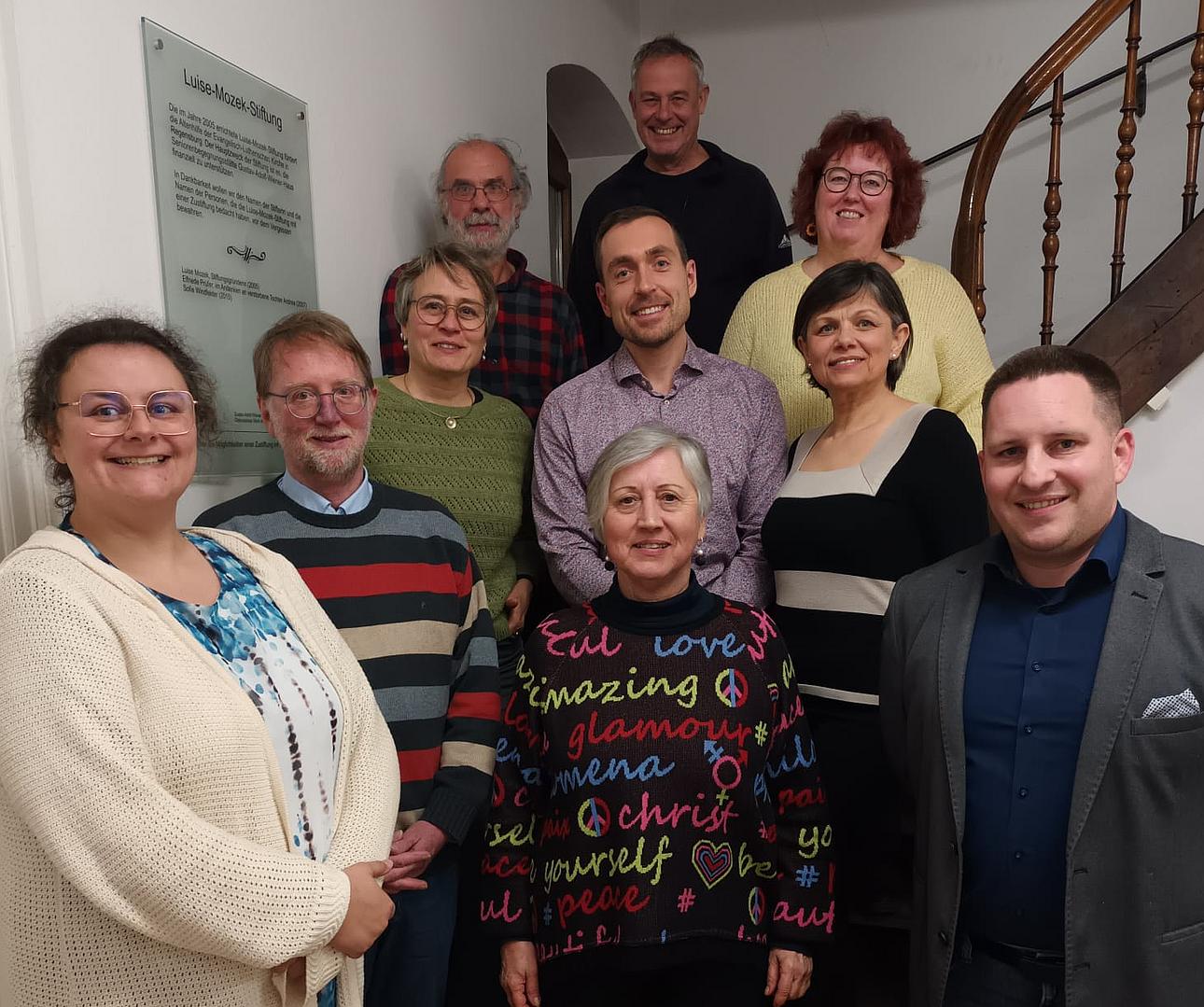 Gruppenfoto von elf Erwachsenen unterschiedlichen Alters, die lächelnd in einem Treppenhaus stehen. Die Gruppe ist der Verwaltungsrat der Diakonie Regensburg.