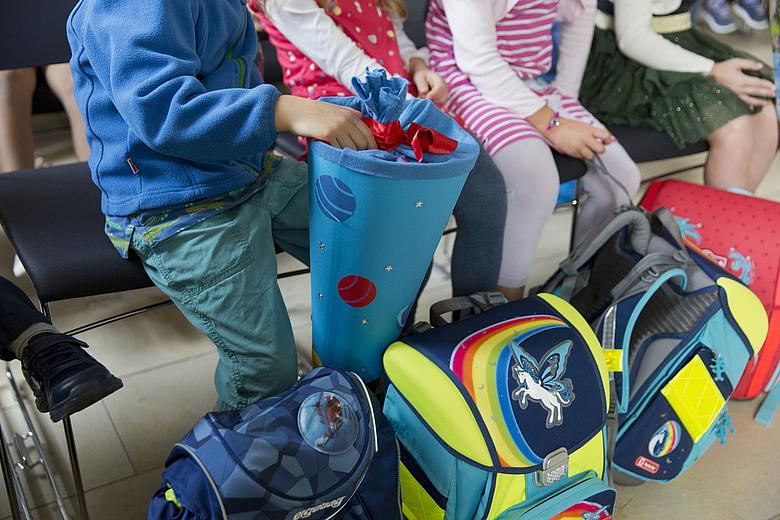 © Rolf Oeser / fundus-medien.de Kinder sitzen mit bunten Schulranzen und einer Schultüte in einem Klassenraum. Es sind nur die Beine und Oberkörper zu sehen, nicht die Köpfe und Gesichter.